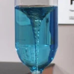 Blue liquid swirling in a clear glass container with a vortex pattern.