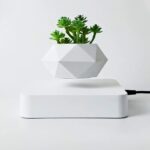 A modern geometric white pot with green succulent plant, placed on a sleek white charging station.