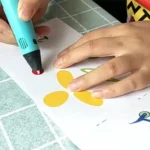 Child's hands creating colorful egg shapes on paper with a blue marker, engaging in a fun and educational craft activity.
