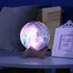 Realistic moon lamp with glowing surface on wooden stand, placed on bedside table next to photo frame in cozy bedroom setting.