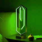 Neon geometric desk lamp with a modern, futuristic design, glowing in vibrant green light, placed on a black table next to a yellow vase and a book.