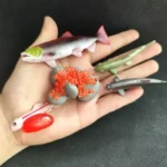 Collection of realistic miniature fish and marine animal models including a red fish, green eel, gray shark, and orange coral, perfect for science education and marine biology projects.