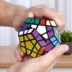 Hand holding a colorful, complex 3D twisty puzzle cube with multiple interconnected segments, showcasing vibrant colors and intricate design.