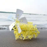 A small yellow wind turbine model with white blades placed on the sandy beach, showcasing renewable energy technology in a natural setting.