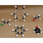 A molecular model kit with black, white, red, and green balls connected by sticks, representing different atoms, on a brown surface.