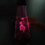 A lava lamp with a glowing plasma ball inside, emitting vibrant purple and pink electrical discharges in a dark setting.