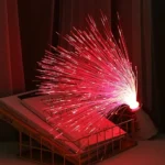 Sparkler firework experiment placed on a bookshelf with books, creating bright red sparks and light effects in a cozy indoor setting.