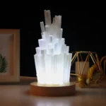 Illuminated crystal sculpture lamp with vertical glass-like prisms on a wooden base, creating a modern and elegant decorative piece.