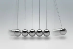 A classic Newton's Cradle with five shiny metal balls suspended by thin wires, demonstrating momentum transfer and energy conservation in physics.