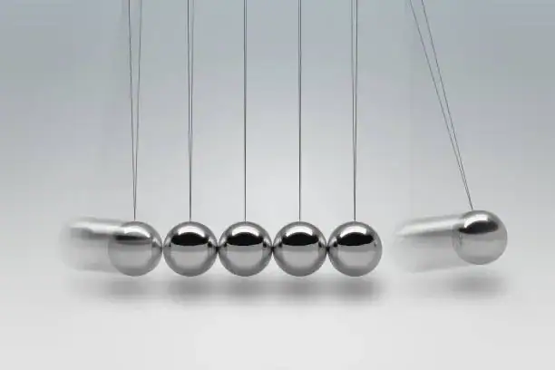 A classic Newton's Cradle with five shiny metal balls suspended by thin wires, demonstrating momentum transfer and energy conservation in physics.
