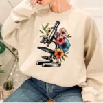 Sweatshirt avec motif de microscope entouré de fleurs colorées, parfait pour les amateurs de science et de décoration originale.