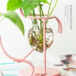 Elegant plant watering system featuring a glass vase and pink metal stand for home decor and plant care.