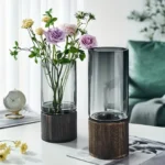 Elegant glass vases with wooden bases, one filled with colorful flowers and the other empty, placed on a white table in a modern living room setting.