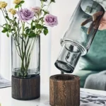 Elegant glass vase with purple roses on a wooden base, showcasing a modern floral arrangement for home decor.