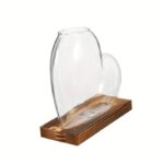 Transparent glass heart-shaped vase displayed on a wooden base, ideal for home decor or as a unique gift.