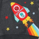 Colorful rocket ship embroidery with dinosaur face and flames on dark fabric background.