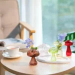 Colorful mushroom-shaped glass vases with flowers arranged on a wooden table, creating a charming and whimsical decor display.