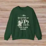 Green sweatshirt featuring a UFO, alien, and astronaut graphic with the text "BEAM ME UP THIS PLACE SUCKS!" for science-themed fashion and humor.